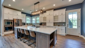 A spacious kitchen with white cabinets, a large island with bar stools, stainless steel appliances, and a pendant light. - Spacious Lake Charles Craftsman - Pet Friendly! (Lake Charles)