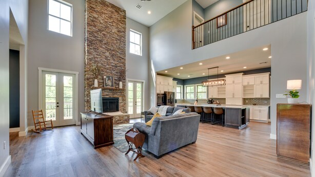 A spacious living area with a stone fireplace, a grey sofa, and a kitchen with white cabinets and a large island. - Spacious Lake Charles Craftsman - Pet Friendly! (Lake Charles)
