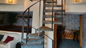 Un escalier en colimaçon, avec un revêtement en pierre et des rampes noires, menant à l’étage supérieur.