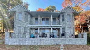 A two-story brick house with a balcony, a front porch with chairs, and a small garden area. - Castle Cove Lakefront Home (Goreville)