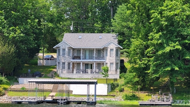 Une maison en pierre à deux étages, dotée d’un quai s’avançant dans un lac, et entourée d’une forêt dense.