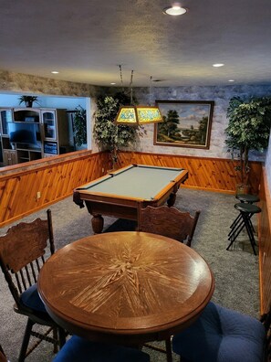 Relax in the lounge area with a pool table, surrounded by comfortable seating and a beautiful landscape painting.
