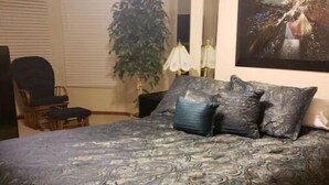 Une chambre avec un grand lit, une chaise, une lampe et une plante.