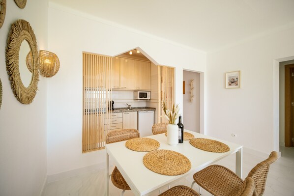 A modern kitchen with wooden cabinets, a microwave, and a dining area with a white table and wicker chairs.