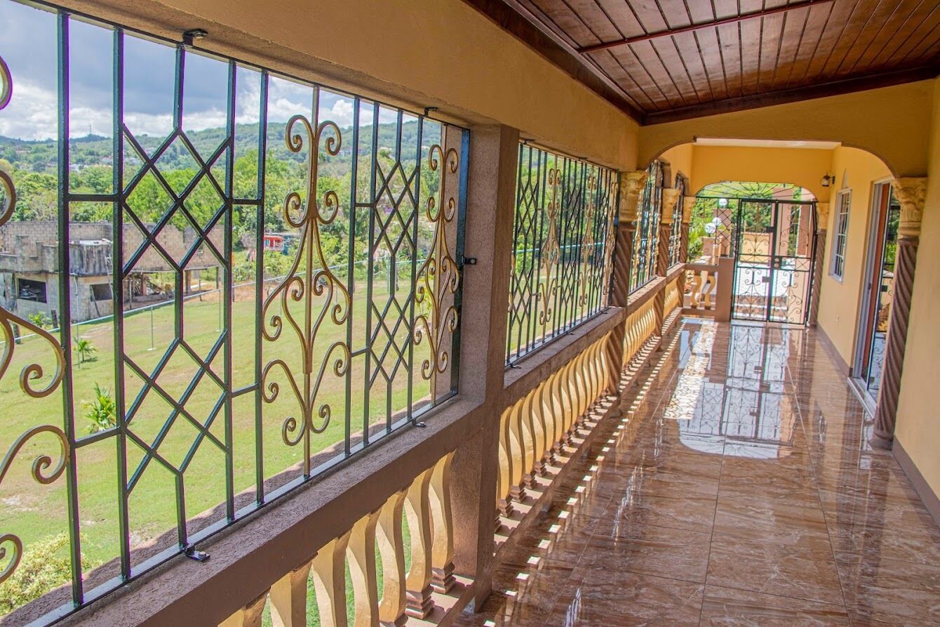 A corridor with a view of a green landscape through ornate metal railings.