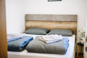Una cama bien tendida con almohadas estampadas y mantas dobladas, un cabecero de madera y una mesita de noche con un jarrón de flores.