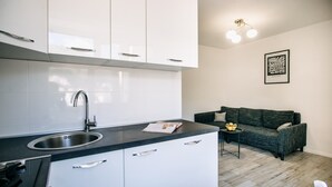 A modern kitchen with white cabinets, a black countertop, and a stainless steel sink. There is a framed artwork on the wall and a dark-colored sofa in the living area. - Apartment Wanda - Two Bedroom Apartment with City View (Dubrovnik)