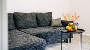A modern living room with a grey sectional sofa, a small round table with a fruit bowl, and a vase with dried branches. - Apartment Wanda - Two Bedroom Apartment with City View (Dubrovnik)