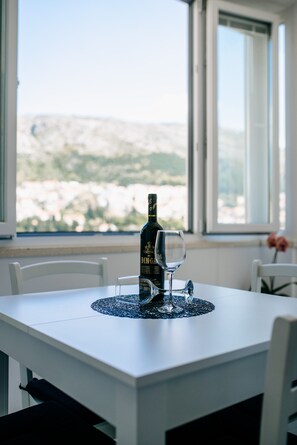 Una mesa de comedor con una botella de vino y una copa, sobre un mantel blanco con un posavasos de encaje.