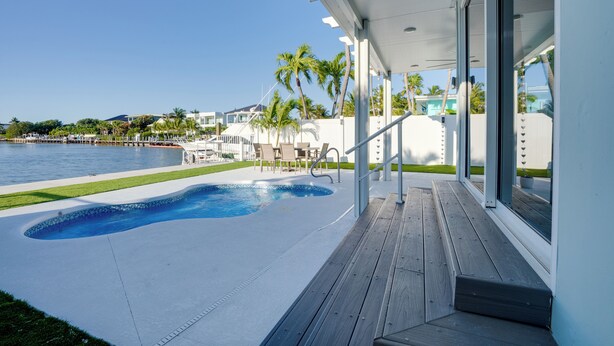 Ein Schwimmbad mit Holzterrasse, einer überdachten Veranda und Blick aufs Meer.