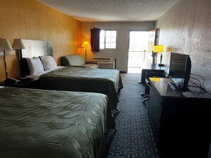A hotel room with two beds, a desk with a computer, a chair, a lamp, and a window with curtains.