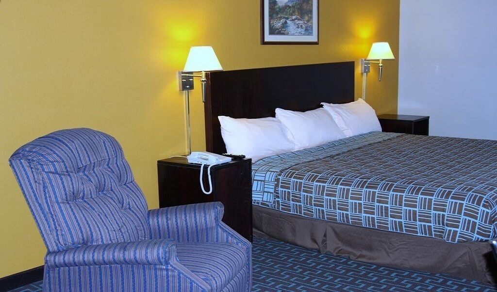 Une chambre d’hôtel avec un lit simple, deux lampes de chevet, une chaise et une table de chevet avec un téléphone.