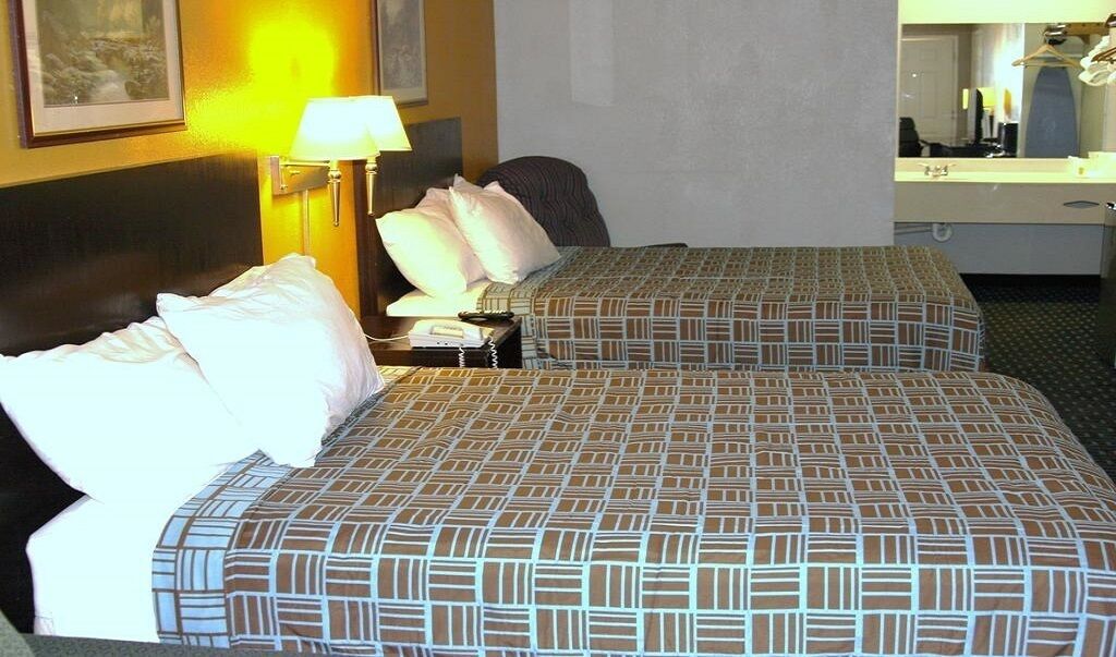 Une chambre d’hôtel avec deux lits, une table de chevet, une lampe, une chaise, un bureau et un miroir.
