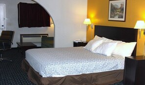 A hotel room with a bed, two bedside lamps, a chair, a desk, and a painting on the wall.