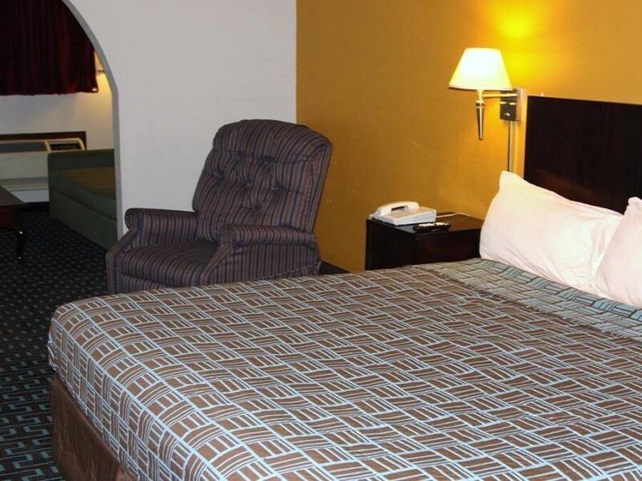 Una habitació d'hotel amb un llit, una cadira, un escriptori, una làmpada i un telèfon.