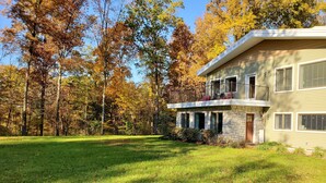 A two-story house with a stone facade, a balcony with red outdoor seating, and a well-maintained lawn. - IU Getaway | Hot Tub, Fire Pit & 10 Min to Campus 3BR, 3BA (Bloomington)