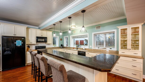 A kitchen with a large island, bar stools, a black refrigerator, a microwave, and a window with blinds. - IU Getaway | Hot Tub, Fire Pit & 10 Min to Campus 3BR, 3BA (Bloomington)