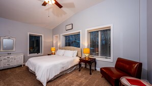 A bedroom with a bed, bedside lamps, a dresser, a red leather chair, and a ceiling fan. - IU Getaway | Hot Tub, Fire Pit & 10 Min to Campus 3BR, 3BA (Bloomington)