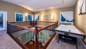 A room with a pool table, a staircase with a wooden railing, and a view of trees through the windows. - IU Getaway | Hot Tub, Fire Pit & 10 Min to Campus 3BR, 3BA (Bloomington)