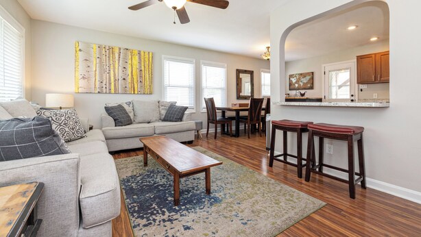 A living room with a sofa, coffee table, and a dining area with chairs and a table. - OPEN 4BR/2BA • Sleeps 8 • Near Hwy • Covered Deck • Close to Downtown & Expo Ctr (Louisville)