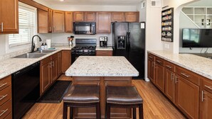A kitchen with wooden cabinets, a granite countertop, a stainless steel sink, a black refrigerator, a stove, and a microwave. - OPEN 4BR/2BA • Sleeps 8 • Near Hwy • Covered Deck • Close to Downtown & Expo Ctr (Louisville)