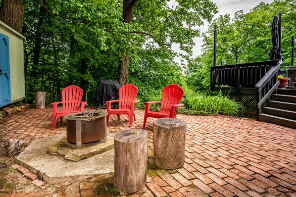 A patio with red chairs, a fire pit, and a wooden deck.
