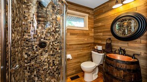 Une salle de bain avec une douche en pierre, un meuble-lavabo en bois avec un évier en cuivre et des toilettes au style rustique.