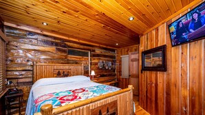 Une chambre de style cabane en bois, avec un lit, un téléviseur fixé au mur et une tête de lit en bois ornée d’un motif d’ours.