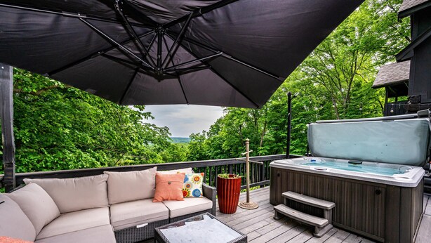 Une terrasse avec un canapé, un jacuzzi et une table placée sous un parasol.