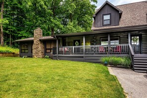 A log cabin with a stone chimney, a covered porch, and a grassy yard. - Romantic Ridge Cabin | Hot Tub, Views & Near Nashville 1BR, 1BA (Nashville)
