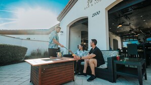 Un espacio al aire libre con una mesa de madera y mobiliario de mimbre en un bar y lounge llamado "Ti Cuba".
