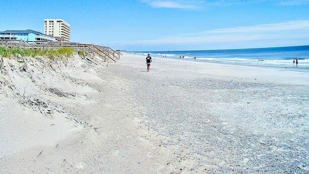A beach with a person walking, a pier, and buildings in the background. - ❤️Amazing Round House, Ground Floor Unit, Easy Walk To The Beach, Self Check-In (Carolina Beach)