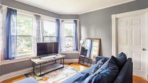 A living room with a large window, a flat-screen TV, a sofa, and a painting on the wall. - Cheney Bros Hill Top Mansion (Manchester)