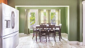 A dining area with a table and chairs, a refrigerator, and a window with curtains. - Cheney Bros Hill Top Mansion (Manchester)