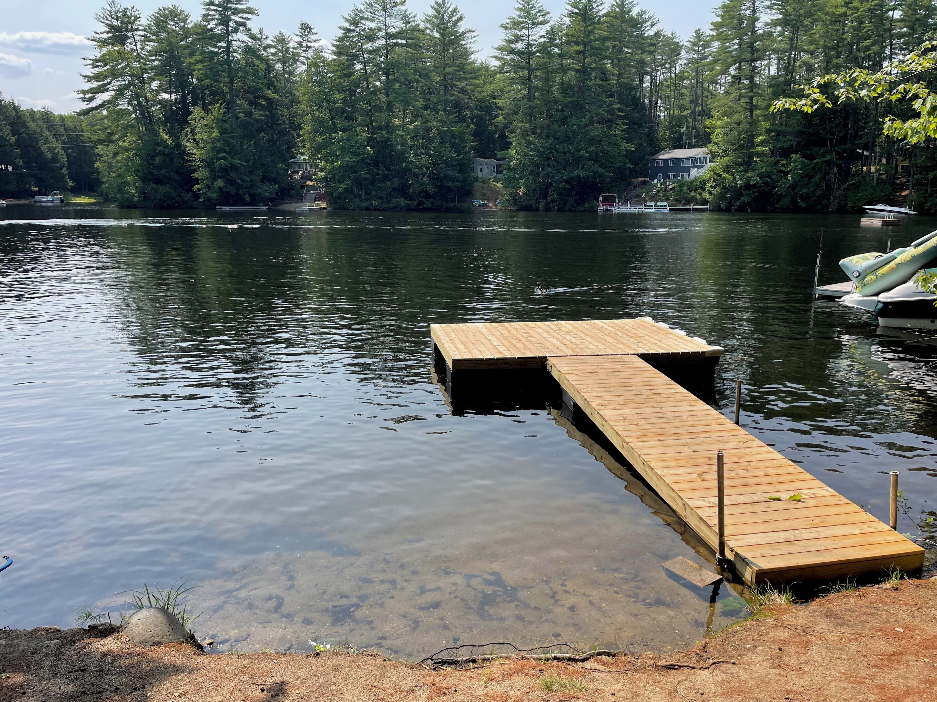 Un muelle de madera se adentra en un lago tranquilo rodeado de un bosque denso.