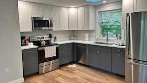 A modern kitchen with grey cabinets, stainless steel appliances, and a skylight.