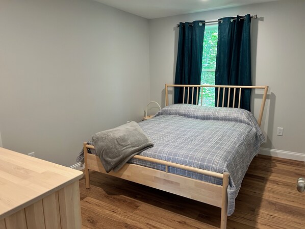 A single bed with a wooden frame, a grey blanket, and a blue and white checkered duvet.