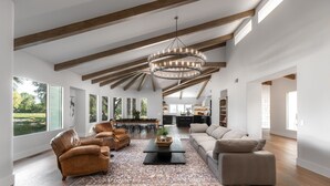 Un vaste salon doté d’un grand plafond en bois, d’un lustre central et offrant une vue sur l’extérieur grâce à de grandes fenêtres.