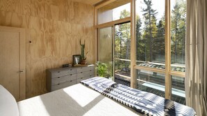 A bedroom with a large window, wooden walls, a bed, a dresser, and a potted plant. - Scandinavian Chalet and sauna in Lutsen - Grey (Lutsen)