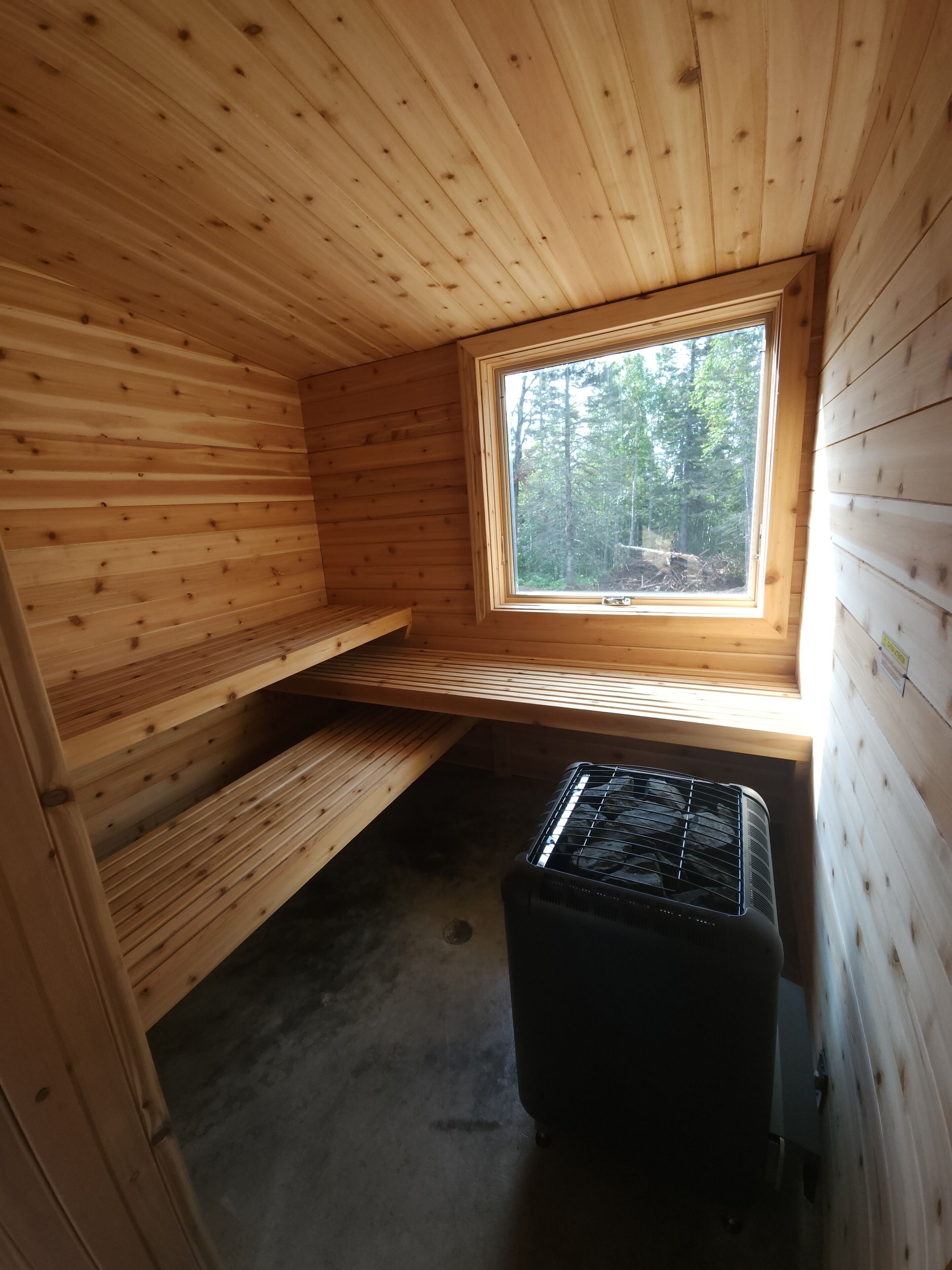 Une petite cabane en bois, avec un toit en pente, une fenêtre et un radiateur noir.