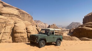 Un vehículo todoterreno verde estacionado en un desierto con grandes formaciones rocosas al fondo.