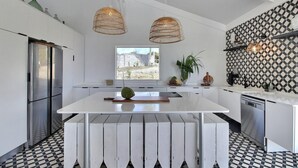 Une cuisine moderne avec des meubles blancs, un îlot central, un réfrigérateur en acier inoxydable, un lave-vaisselle et un pare-feu décoratif.