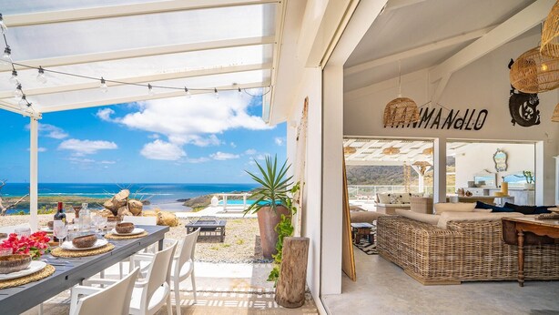 Une villa située sur la côte, dotée d’un coin repas avec vue sur la mer, d’un salon meublé de meubles en osier et offrant une vue sur l’océan.