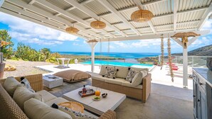 Un espace extérieur aménagé, abrité et doté de sièges, avec vue sur la piscine, du mobilier en osier et des décorations suspendues.