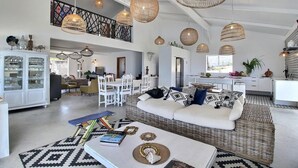 Un vaste espace de vie doté d’un haut plafond, de meubles en osier et d’un coin repas avec des chaises blanches.