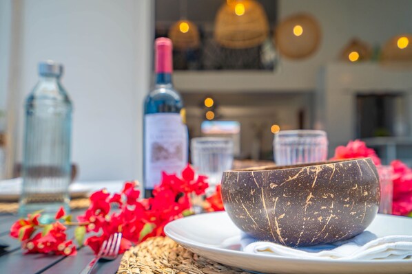 Una mesa de comedor con un cuenco de mármol oscuro, una botella de vino y flores rojas.