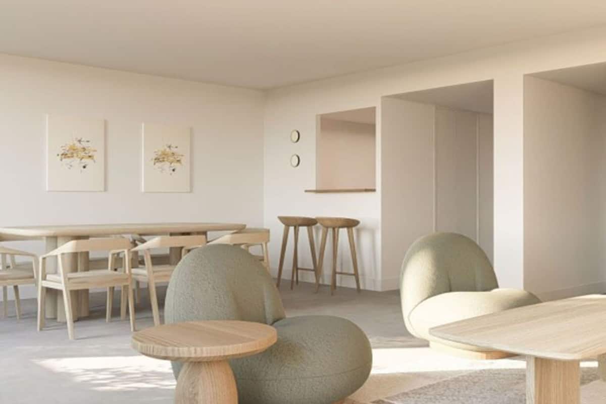 Un salon moderne et minimaliste, doté d’une table à manger en bois, de deux petites tables d’appoint rondes et d’un coin salon confortable avec un canapé et des fauteuils.