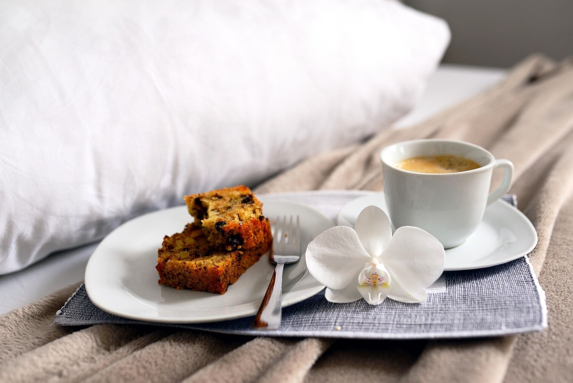 Ein Stück Kuchen auf einem weißen Teller, eine Tasse Kaffee auf einem Untertasse und eine weiße Orchidee auf einer blauen Serviette.