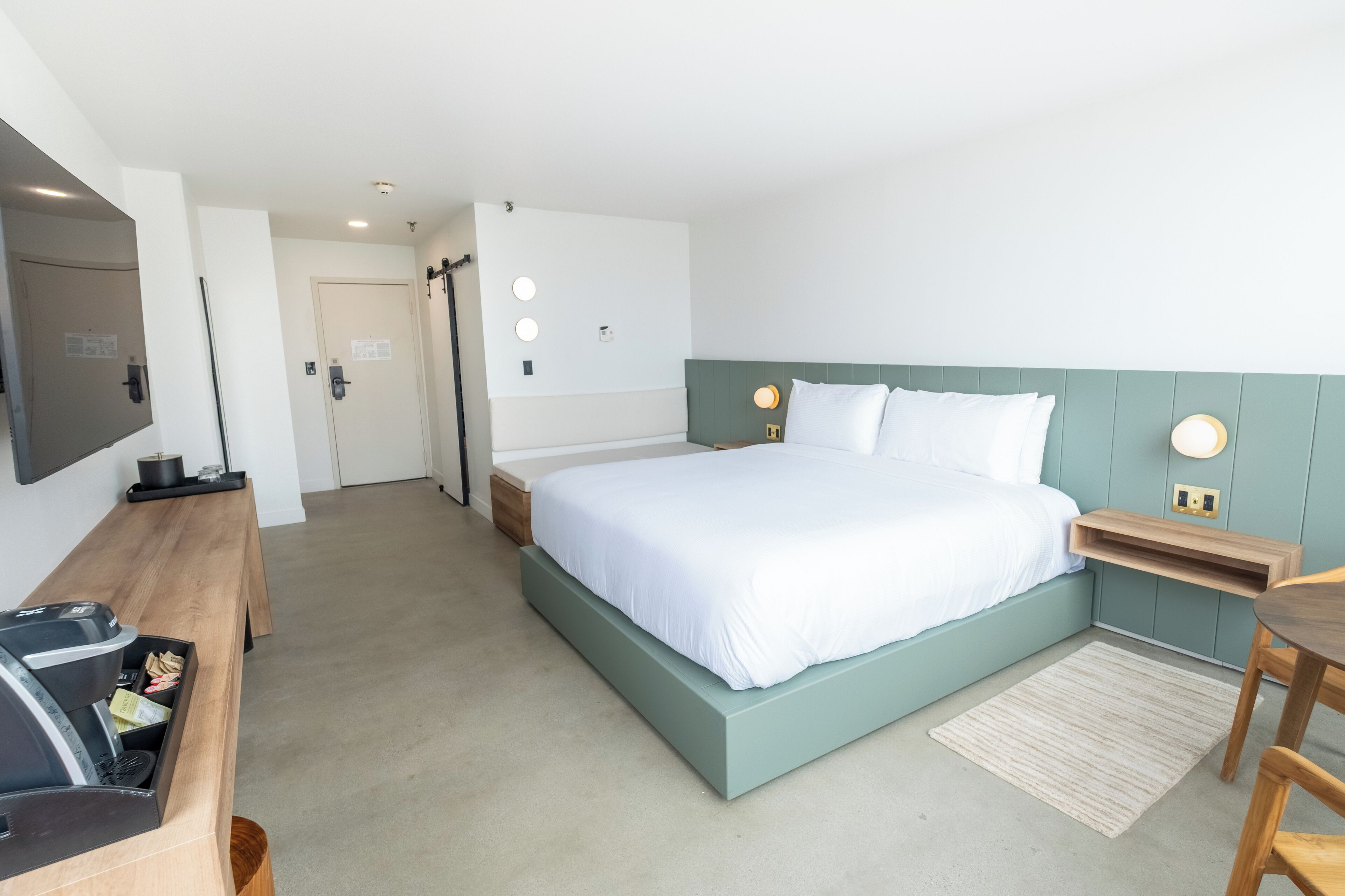 A modern hotel room with a large bed, a desk, a television, and a small table.