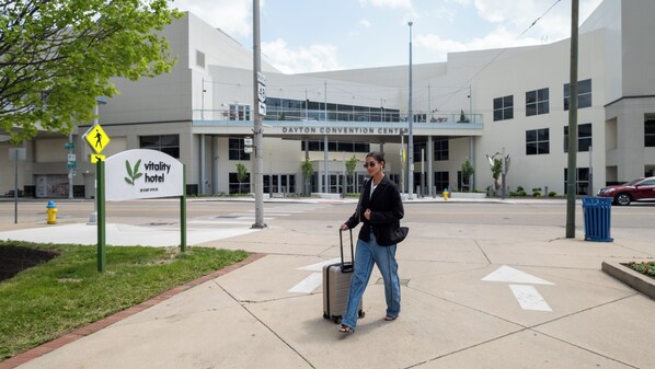 A hotel sign with a pedestrian crossing symbol, a building with a convention center sign, and a person with a suitcase on a sidewalk.